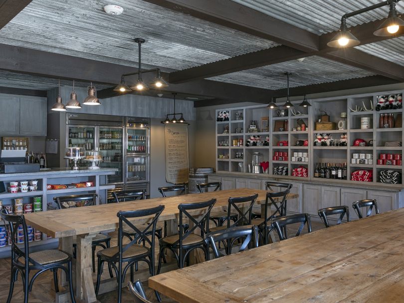 A rustic cafe or brewery with long wooden tables, metal chairs, open shelves stocked with drinks and gear, a cool industrial vibe, and warm lighting.