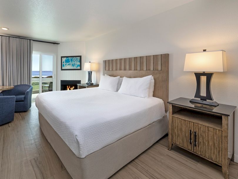 A tidy hotel room with a large bed, two nightstands, a lamp, a sofa, and a desk by the window, bright and modern.