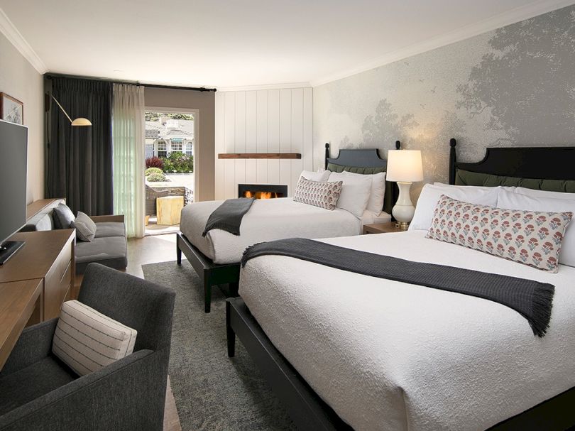 A modern hotel room with two queen beds, gray accents, a seating area, a desk, and a balcony door to an outdoor space.