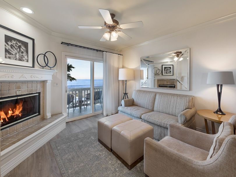 Cozy coastal living room with a gas fireplace, beige furniture, sliding glass doors to a balcony and ocean view, soft lighting, and a large mirror.
