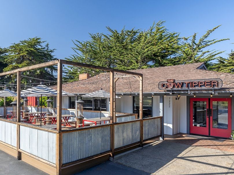 A small outdoor dining area attached to a rustic restaurant with a wooden fence, red doors, and blue sky above.