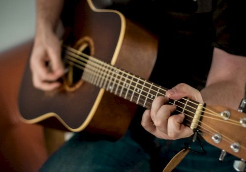 A close-up of someone playing a brown acoustic guitar, fingers strumming the strings.