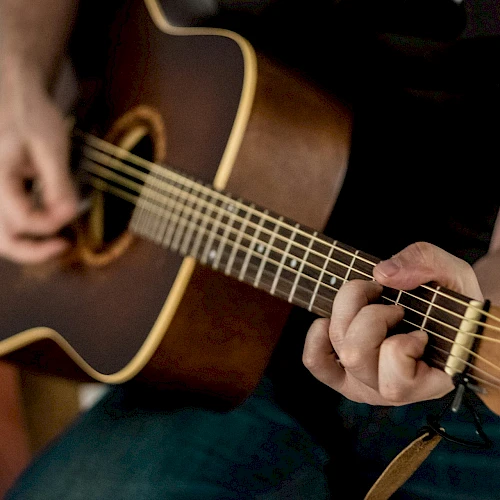 A close-up of someone playing a brown acoustic guitar, fingers strumming the strings.