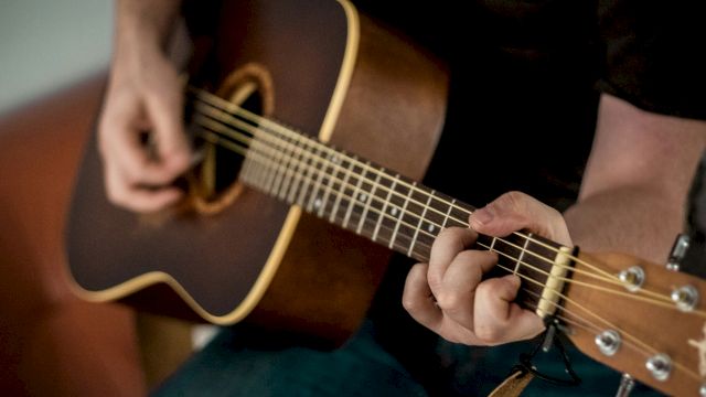 A close-up of someone playing a brown acoustic guitar, fingers strumming the strings.