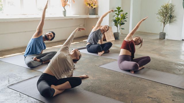 People doing a yoga class in a bright studio, various seated side stretches on mats with blocks nearby.