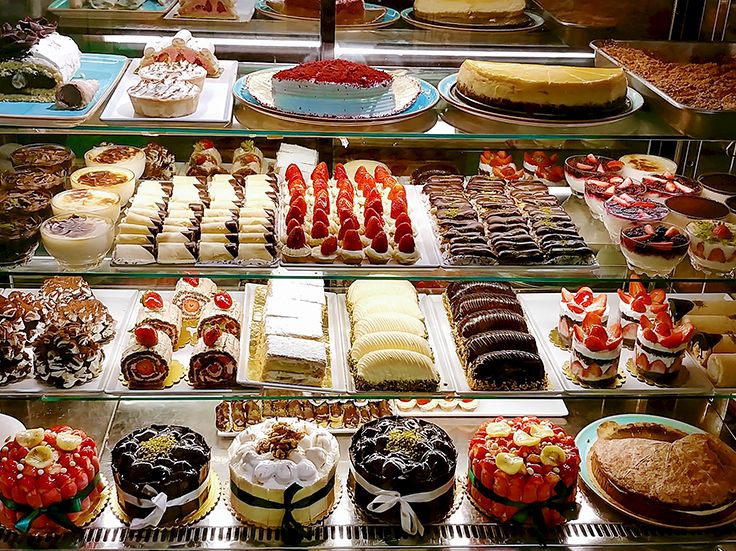 Assorted pastries and cakes in a bakery display: mini tarts, cream puffs, eclairs, slice cakes, and chocolate desserts, all arranged neatly.