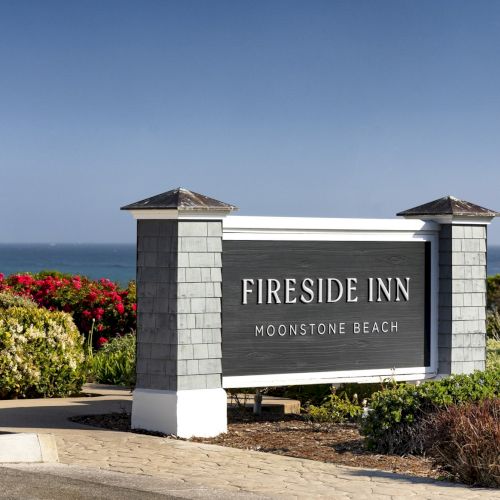 A roadside sign reads &ldquo;Fireside Inn Moonstone Beach&rdquo; with ocean view and colorful bushes along the doorway.