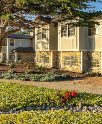 A sunny residential building with a well-kept lawn, stone walkway, and trees framing a cozy courtyard area.